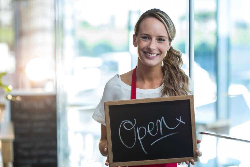 Portrait of smiling waitress showing slate with open sign in cafe