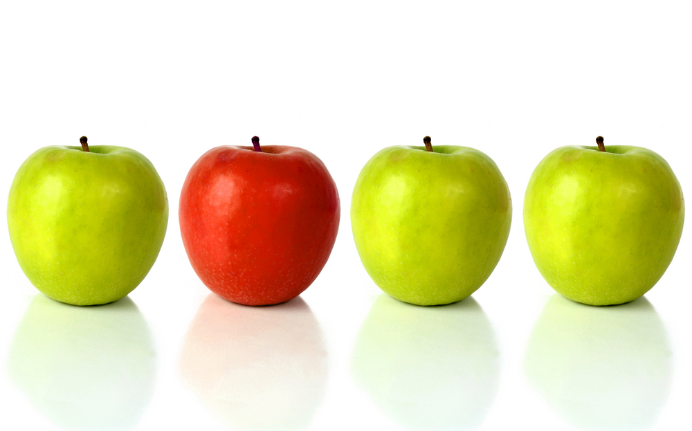 green apple with the red one standing out from the crowd - over a white background with reflection